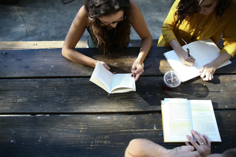Dos personas estudiando con libros y cuaderno sobre una mesa de madera