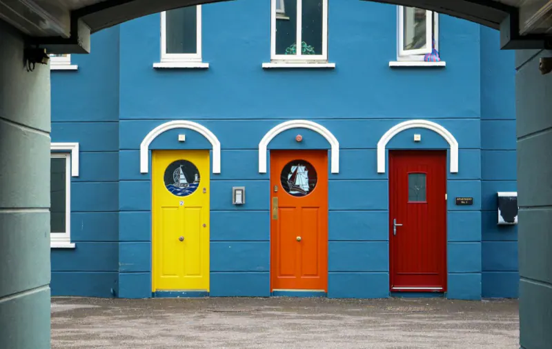 Three doors painted yellow, orange and red on a blue facade