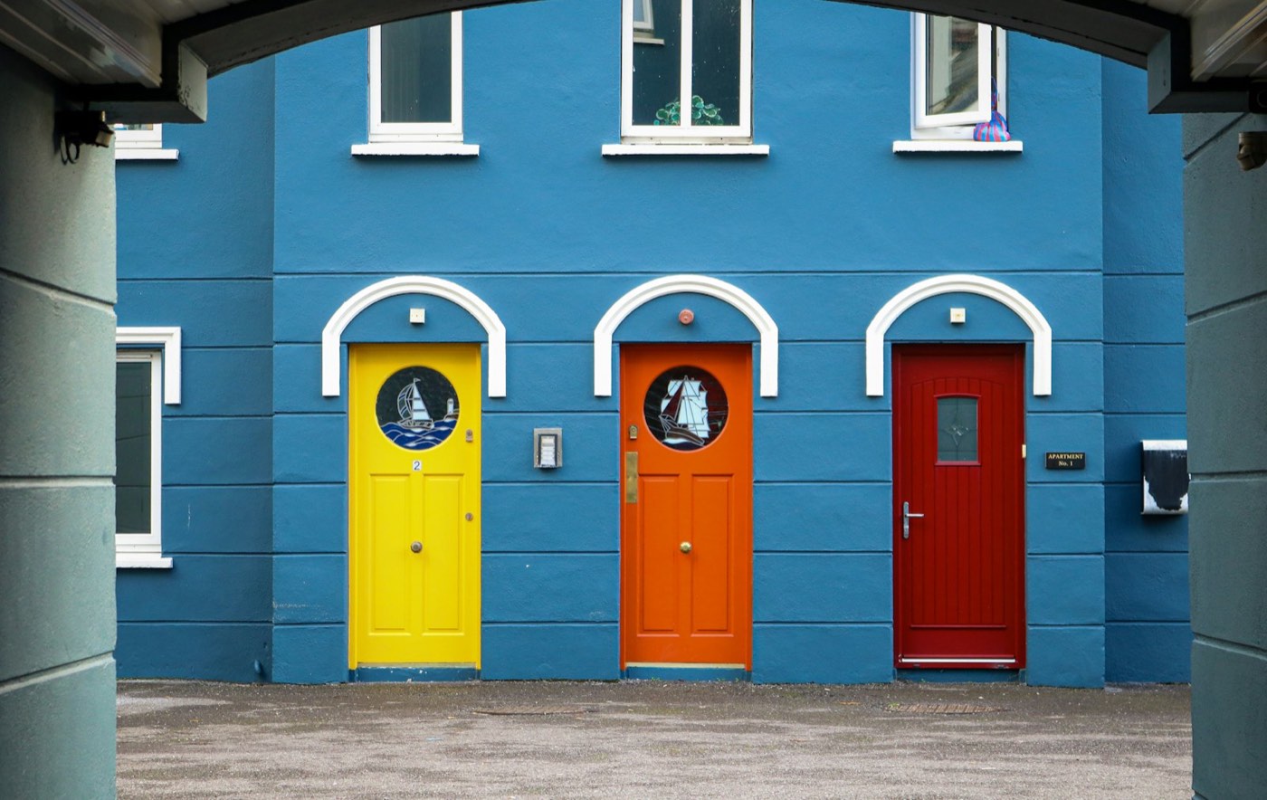 Tres puertas de colores amarillo, naranja y rojo en una fachada azul
