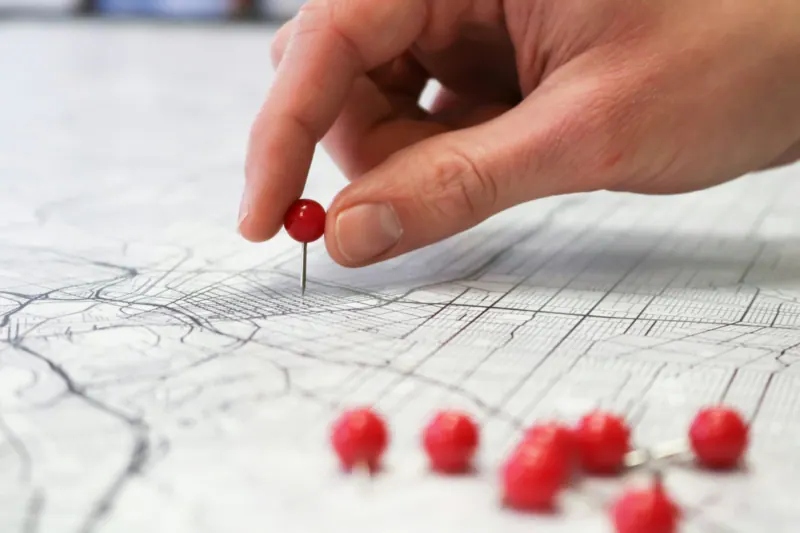 Mano colocando un alfiler rojo sobre un mapa impreso de una ciudad