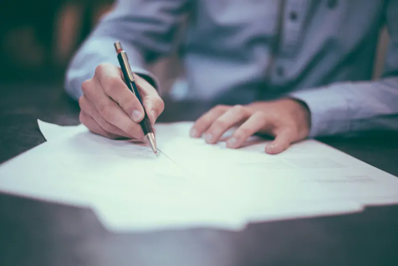 Person signing a paper contract at a desk with a pen