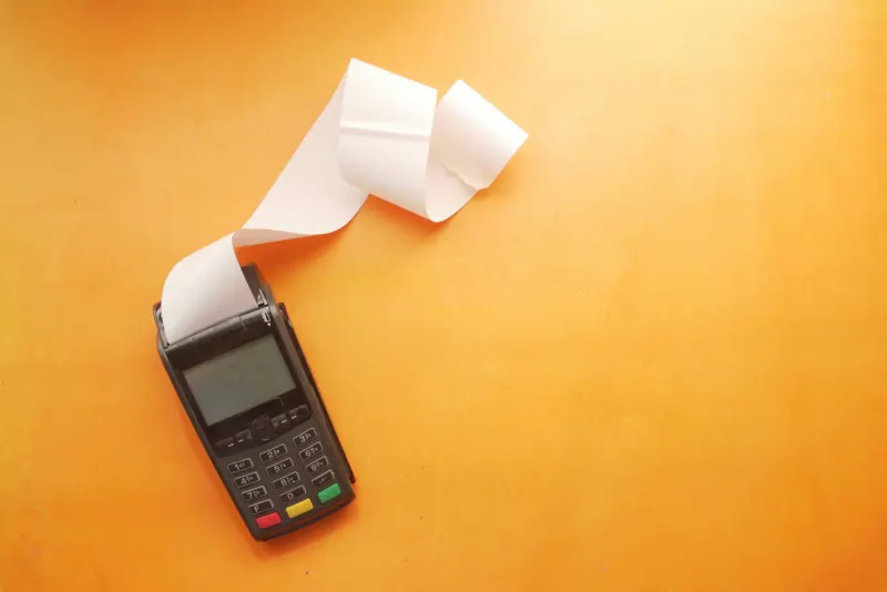A payment terminal with a long paper receipt coming out against an orange background