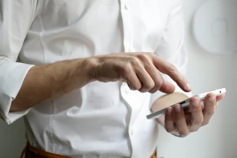 Persona con camisa blanca usando un teléfono inteligente con la mano