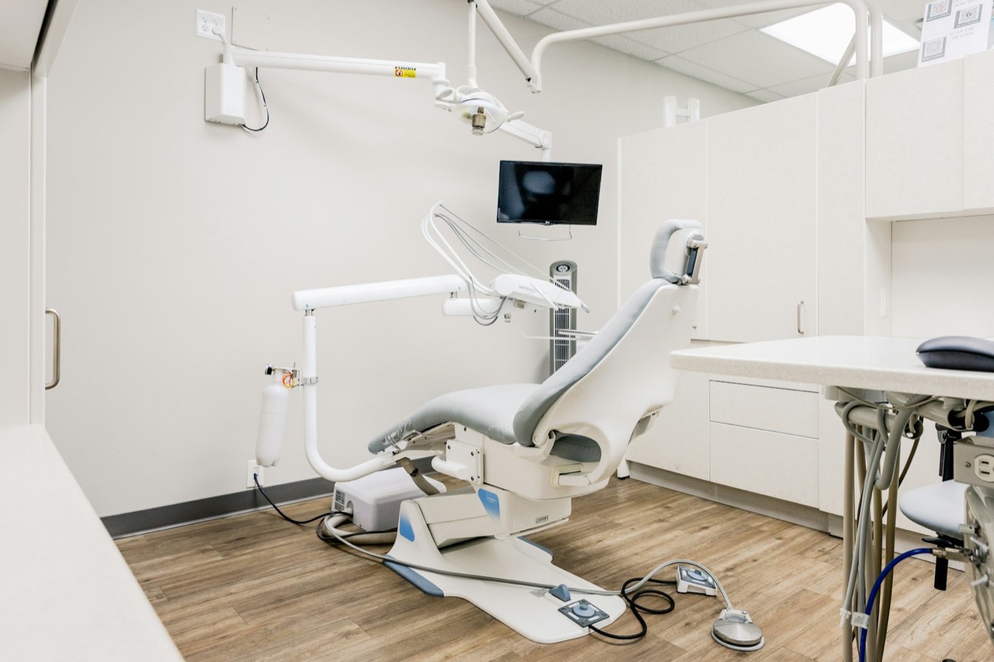 Clean, well-lit dental office with a patient chair, overhead lamp and monitor