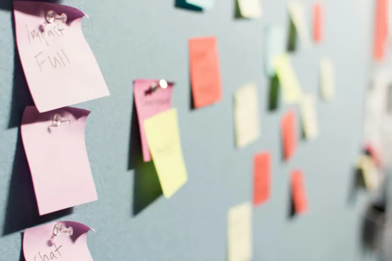 Notas adhesivas de colores clavadas en un tablero de corcho para organizar tareas