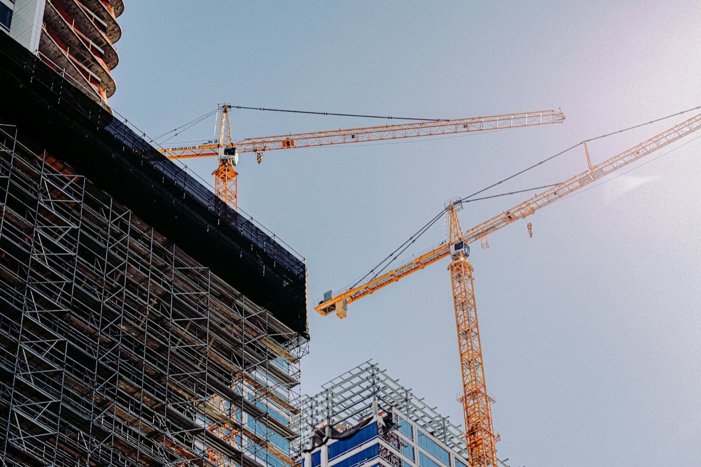 Yellow tower cranes next to a building under construction with scaffolding