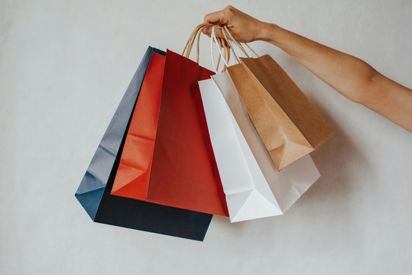 Mano sosteniendo varias bolsas de compras de colores sobre fondo blanco