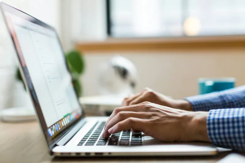 Hands typing on the keyboard of a silver laptop on a desk