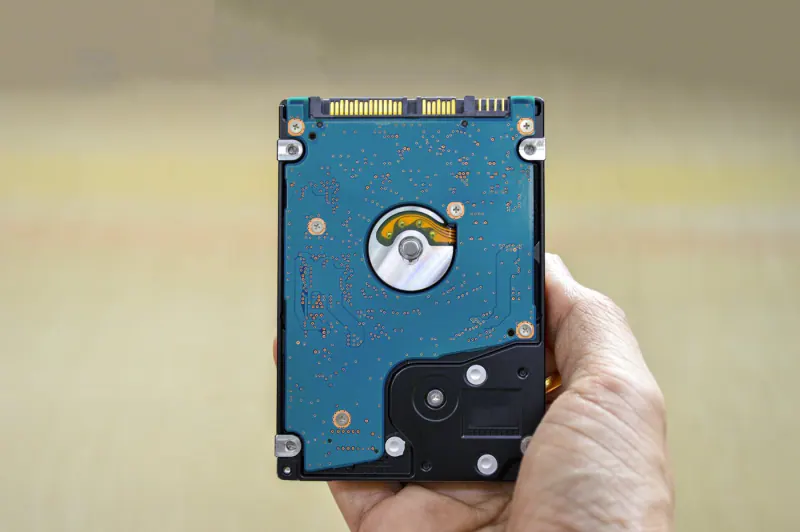 Mano sosteniendo un disco duro de 2.5 pulgadas visto por su circuito