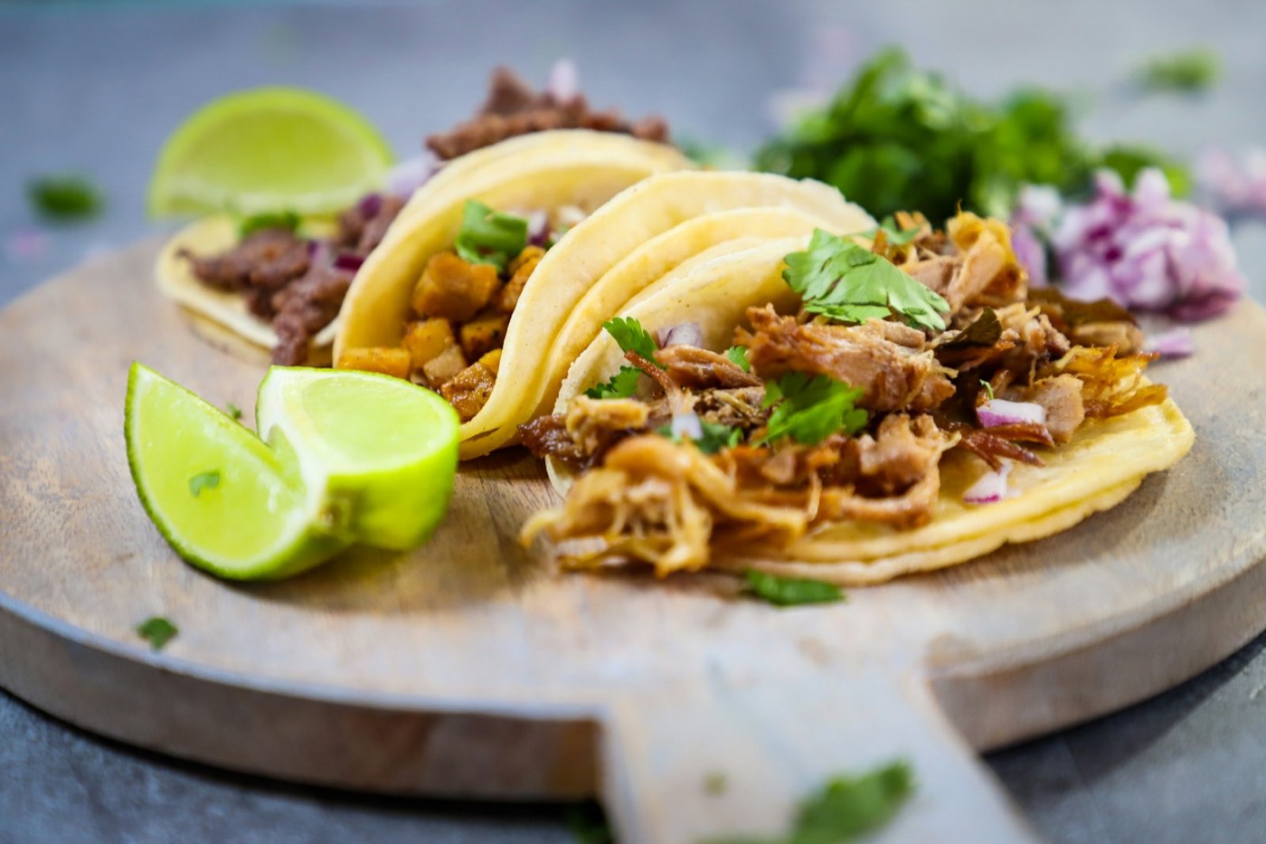 Three beef tacos with cilantro, red onion and lime on a wooden board