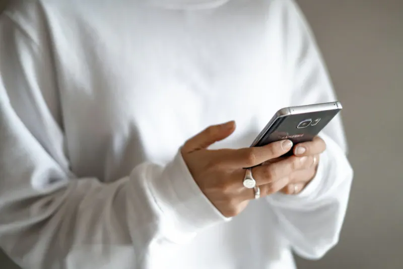 Manos de una persona con suéter blanco escribiendo un mensaje en su teléfono