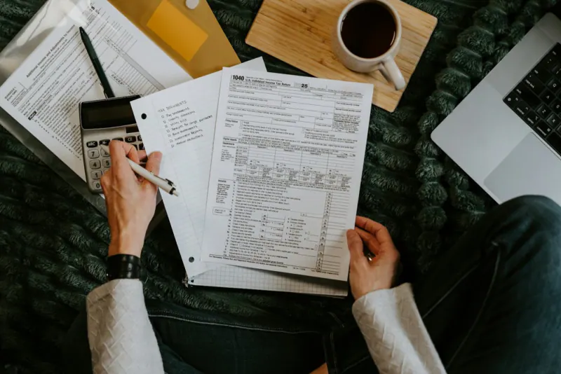 Person reviewing tax documents with a calculator and laptop to issue invoices