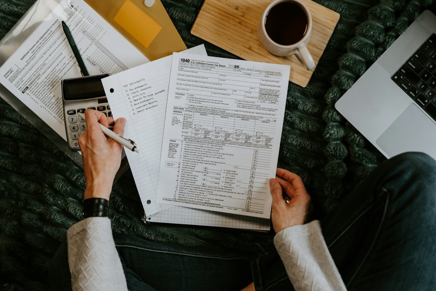 Person reviewing tax documents with a calculator and laptop to issue invoices