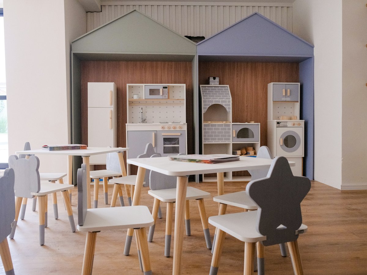 Salón de preescolar con mesas pequeñas y cocinita de juego