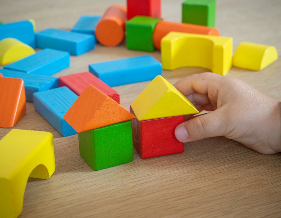 Mano de un niño construyendo con bloques de madera de colores