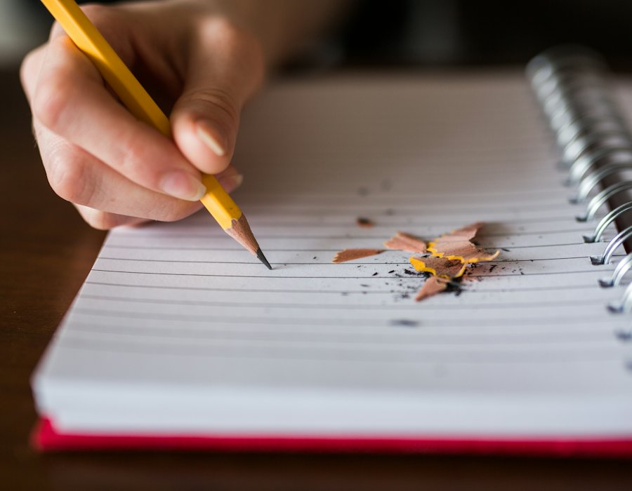 Mano escribiendo con lápiz en un cuaderno de espiral