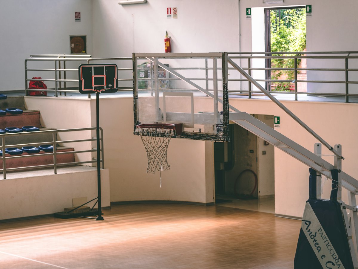 Gimnasio techado con duela, tablero de básquetbol y gradas