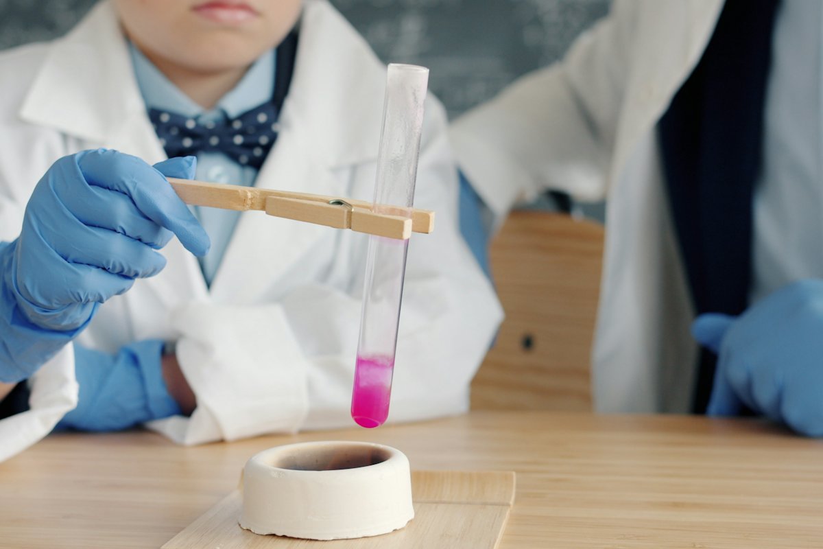 Alumno con bata y guantes sostiene un tubo de ensayo en el laboratorio