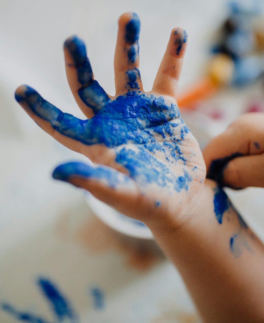 Mano de un niño cubierta de pintura azul durante una clase de arte