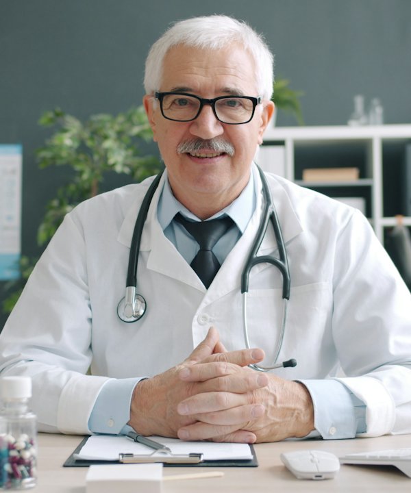 Médico de cabello canoso con bata blanca, sentado en su consultorio