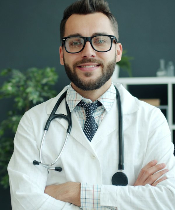 Médico con lentes y bata blanca, de brazos cruzados en su consultorio