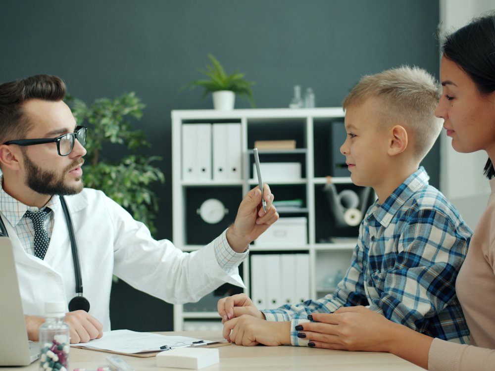 Pediatra revisando a un niño mientras su mamá lo acompaña