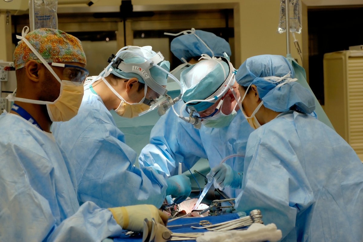 Equipo de cirujanos con uniforme azul operando bajo lámparas quirúrgicas