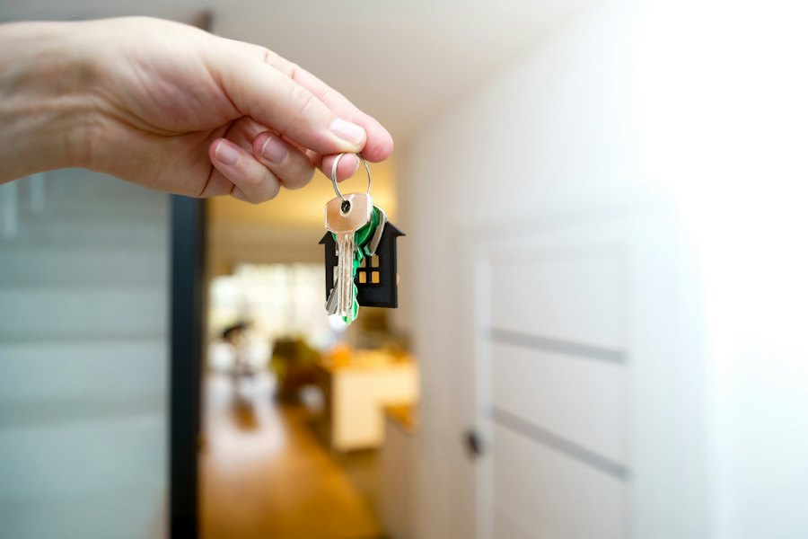 Mano sosteniendo las llaves de una casa frente a la puerta