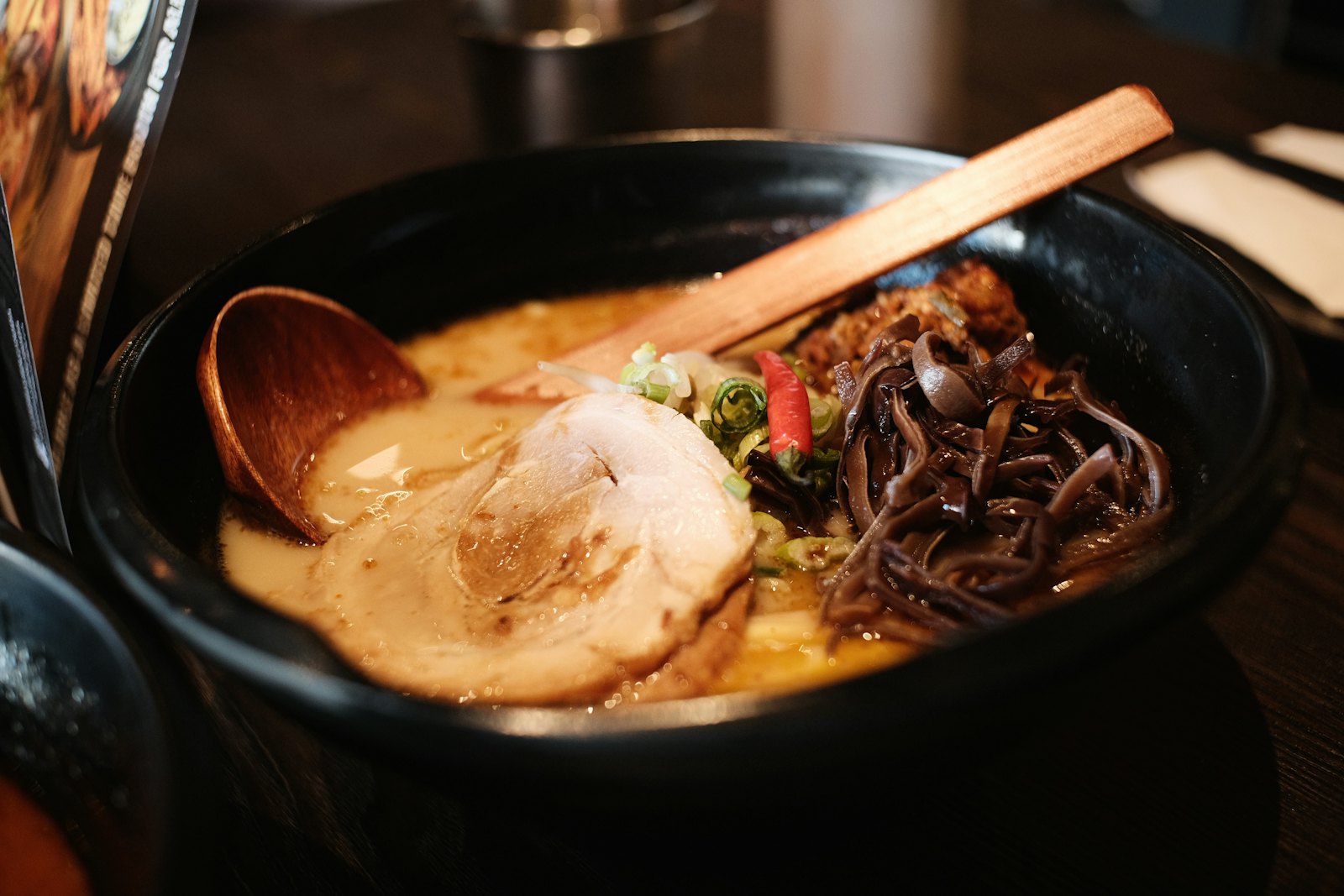 Tazón de ramen tonkotsu con chashu, huevo y fideo sobre mesa oscura