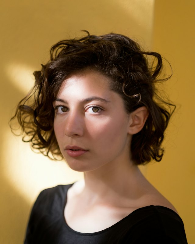 Mujer de cabello rizado corto sobre fondo ocre