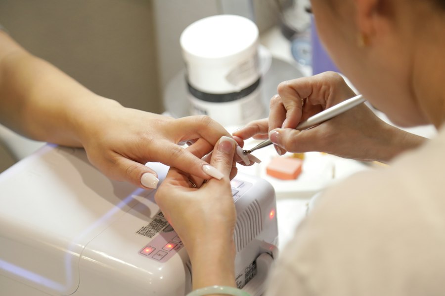 Manicurista trabajando las uñas de una clienta junto a la lámpara de secado