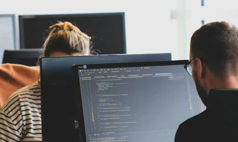 Dos desarrolladores programando un sistema a la medida frente a monitores con código